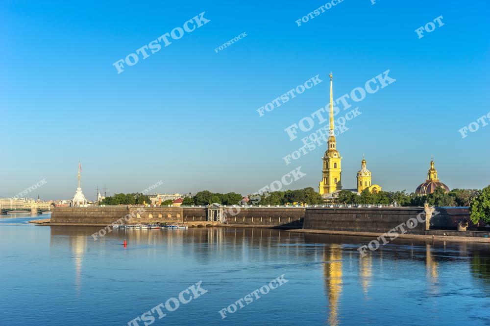 Раннее утро в Санкт-Петербурге с видом на Петропавловскую крепость. Первые солнечные лучи освещают крепостные стены, шпиль собора и набережную Невы, создавая атмосферный городской пейзаж северной столицы России. Фотография подчёркивает историческое наследие, архитектурное величие крепости и спокойную атмосферу раннего утра. Изображение идеально подходит для публикаций о путешествиях по России, архитектуре Санкт-Петербурга, панорамных видах города и достопримечательностях Петербурга.